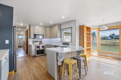 Kitchen featuring gray cabinetry, a peninsula, backsplash, stainless steel appliances, and light wood-style flooring