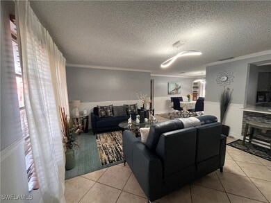 Living room with a stone fireplace, light tile patterned floors, a textured ceiling, and ornamental molding
