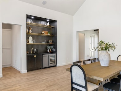 Dining room with light wood-style floors, bar with sink, beverage cooler, and high vaulted ceiling