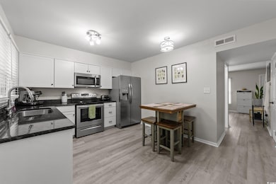 Kitchen with appliances with stainless steel finishes, a sink, light wood-type flooring, and white cabinets