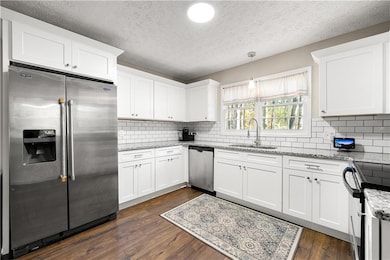Kitchen featuring stainless steel appliances, light stone countertops, a textured ceiling, white cabinets, and dark wood-type flooring