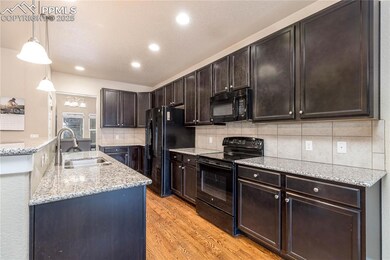Kitchen featuring a breakfast bar, pendant lighting, light granite counters, black appliances, and a center island with sink.