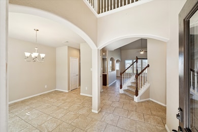 This photo showcases a bright, open entryway with elegant tile flooring and high ceilings. An arched doorway leads to a spacious living area, and a staircase with wooden railings adds a touch of sophistication. The adjacent room features a chandelier, ideal for dining.