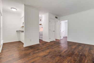 Unfurnished living room featuring dark wood-type flooring and ornamental molding