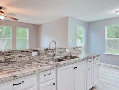 Kitchen with white cabinets, baseboards, a sink, a ceiling fan, and light stone countertops