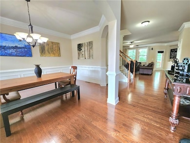 Dining space with stairway, ornamental molding, light wood-type flooring, a wainscoted wall, and a ceiling fan