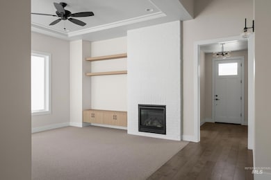 Unfurnished living room featuring a raised ceiling, a fireplace, wood finished floors, a ceiling fan, and carpet