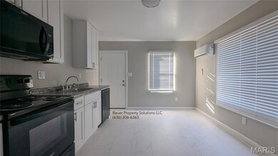 Kitchen with black appliances, white cabinets, and light marble finish flooring
