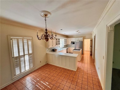 Kitchen featuring ornamental molding, light tile patterned floors, glass insert cabinets, a chandelier, and light countertops