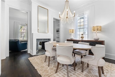 Dining space featuring a chandelier, dark wood-style floors, a multi sided fireplace, crown molding, and built in shelves