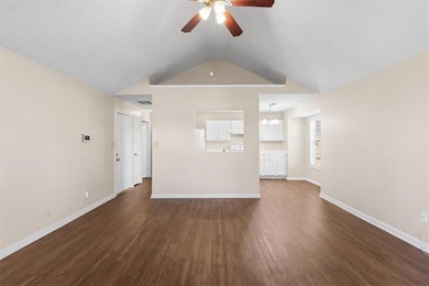 Unfurnished living room featuring dark wood finished floors, vaulted ceiling, a ceiling fan, and a chandelier