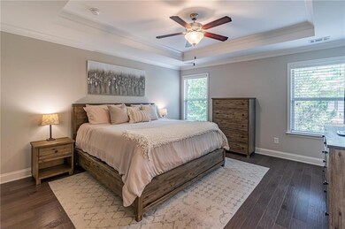 Bedroom with a raised ceiling, baseboards, ornamental molding, dark wood-style flooring, and a ceiling fan