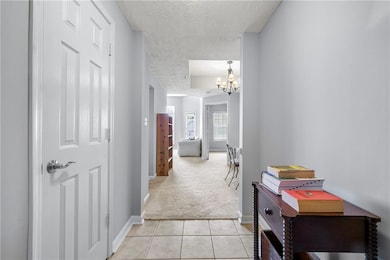 Corridor featuring a textured ceiling, light carpet, light tile patterned floors, and a chandelier