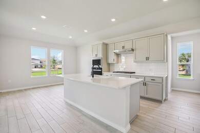 Kitchen with recessed lighting, a center island with sink, decorative backsplash, light stone countertops, and light wood-type flooring