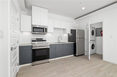 Kitchen with tasteful backsplash, sink, stacked washer and clothes dryer, white cabinetry, and stainless steel appliances