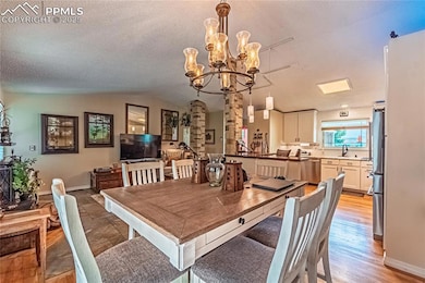 Dining area featuring a chandelier, decorative columns, vaulted ceiling, and wood floors
