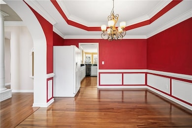 Unfurnished dining area with arched walkways, a raised ceiling, dark wood finished floors, decorative columns, and crown molding
