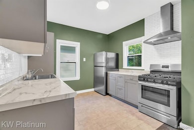 Kitchen featuring decorative backsplash, appliances with stainless steel finishes, wall chimney range hood, and gray cabinets