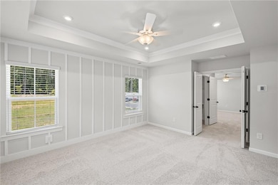 Empty room with a raised ceiling, light carpet, a ceiling fan, recessed lighting, and ornamental molding