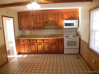 Kitchen with white appliances, sink, ceiling fan, wooden walls, and beam ceiling