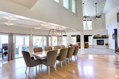 Dining room with light wood-style flooring, a stone fireplace, a towering ceiling, coffered ceiling, and a chandelier