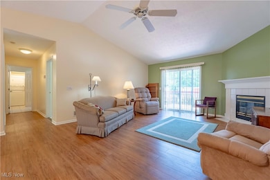 Living room with light wood-type flooring, vaulted ceiling, a ceiling fan, and a tiled fireplace