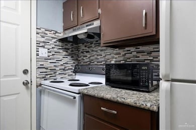 Kitchen featuring under cabinet range hood, white appliances, tasteful backsplash, and dark brown cabinets