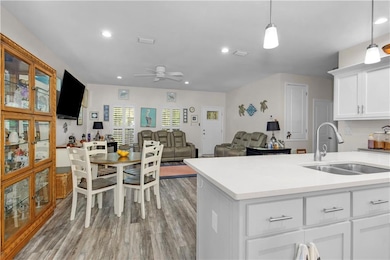 Kitchen featuring a sink, a ceiling fan, light countertops, light wood-type flooring, and white cabinetry