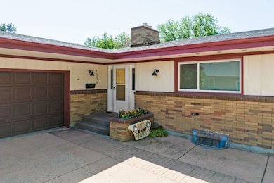 View of front facade with brick siding, a garage, a chimney, and driveway