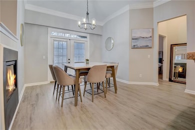 Dining room featuring ornamental molding, light wood-type flooring, a glass covered fireplace, and French doors leading to the balcony