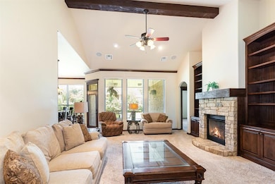 Living area with high vaulted ceiling, carpet flooring, a stone fireplace, ceiling fan, and beamed ceiling