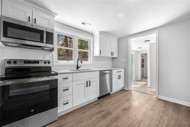 Kitchen featuring stainless steel appliances, light wood-style flooring, light countertops, white cabinets, and decorative backsplash