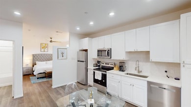 Kitchen with appliances with stainless steel finishes, white cabinets, decorative backsplash, light wood-style floors, and a ceiling fan