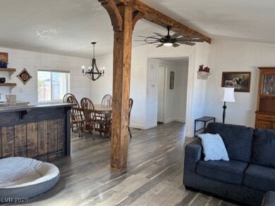 Living room with dark wood-type flooring, vaulted ceiling with beams, and ceiling fan with notable chandelier