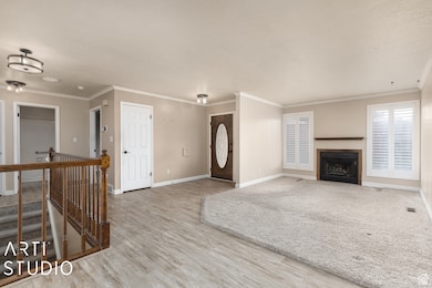Unfurnished living room featuring a fireplace with flush hearth, ornamental molding, and light wood-type flooring