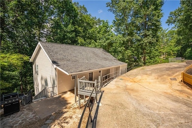View of front facade featuring a shingled roof, concrete driveway, and view of wooded area