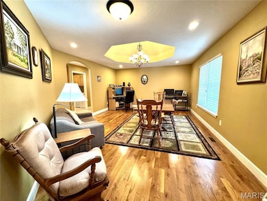 Dining space with arched walkways, light wood-type flooring, a desk, a tray ceiling, and a chandelier