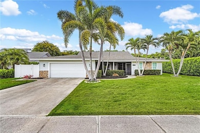 Ranch-style home featuring concrete driveway, stone siding, an attached garage, fence, and a front lawn