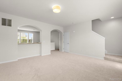 Empty room with light colored carpet, arched walkways, stairway, and recessed lighting
