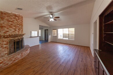 This spacious living room features a high vaulted ceiling and a charming brick fireplace. The laminate wood flooring adds warmth, while large windows provide ample natural light. A ceiling fan enhances comfort, and there's a convenient transition to the adjoining dining area.
