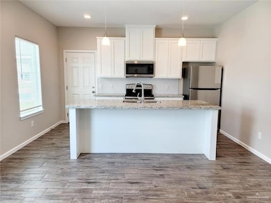 Kitchen with white cabinets, a kitchen island with sink, stainless steel appliances, a sink, and backsplash