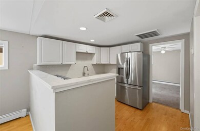 Kitchen with light wood finished floors, stainless steel fridge, white cabinetry, a peninsula, and recessed lighting