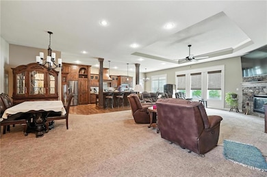Living room featuring a chandelier, a tray ceiling, light carpet, a fireplace, and recessed lighting