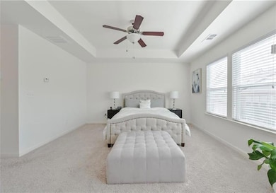 Carpeted bedroom featuring a tray ceiling, baseboards, and a ceiling fan