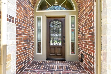 The welcoming front stained and iron door with keyless entry opens onto a patio featuring charming brick flooring, creating a warm and inviting space.