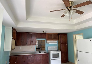 Kitchen with ceiling fan, white appliances, a raised ceiling, and sink