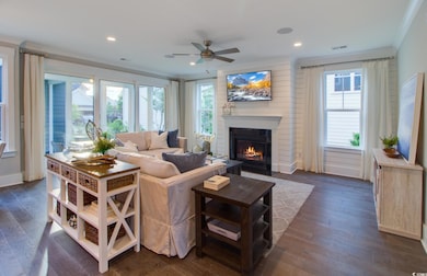 Living room featuring crown molding, a glass covered fireplace, ceiling fan, dark wood finished floors, and recessed lighting