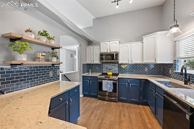 Kitchen featuring stainless steel appliances, blue cabinets, white cabinetry, open shelves, and a towering ceiling