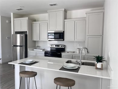 Kitchen with appliances with stainless steel finishes, a kitchen bar, light stone counters, wood finished floors, and white cabinetry