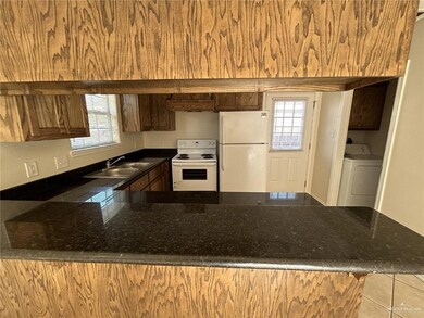 Kitchen featuring a sink, white appliances, dark stone countertops, a peninsula, and washer / dryer